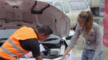 Male car insurance agent going over the car repair parts of the car with the female car owner on a raining day