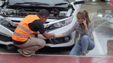 Unhappy Asian woman signing the insurance claim report form from a male car insurance agent in front of her car on a raining day