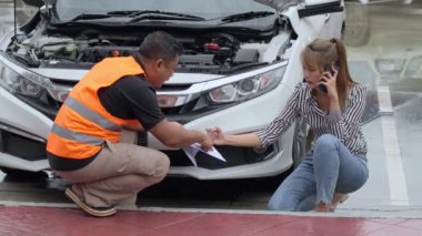 Unhappy Asian woman signing the insurance claim report form from a male car insurance agent in front of her car on a raining day