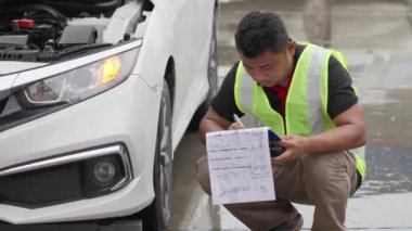 Male car insurance agent or auto mechanic inspecting a car for a car insurance claim at a roadside on a raining day