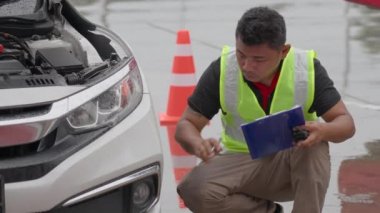 Male car insurance agent or auto mechanic inspecting a car for a car insurance claim at a roadside on a raining day