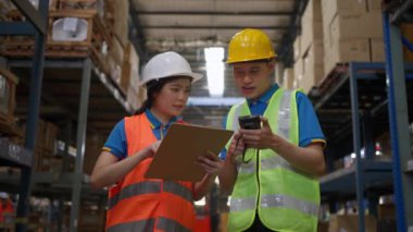 Two happy male and female warehouse staff wearing safety vest and hardhat working together to check the inventory inside the warehouse, happily shaking hands after finish  the task