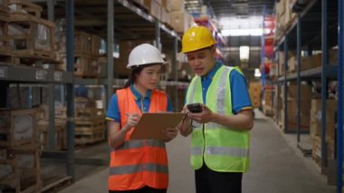 Two happy male and female warehouse staff wearing safety vest and hardhat working together to check the inventory inside the warehouse, giving each other high five after successfully complete the task