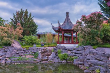 Çin bahçesi. Ebedi Mutluluk Bahçesi, insan ve doğa arasındaki uyum. Su, taşlar, binalar, yollar ve dinlenmek ve dinlenmek için dekoratif tasarım elementleriyle bir bahçe manzarası.
