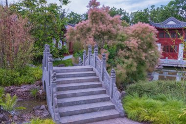 Çin bahçesi. Ebedi Mutluluk Bahçesi, insan ve doğa arasındaki uyum. Su, taşlar, binalar, yollar, dinlenmek ve dinlenmek için dekoratif tasarım elementleri olan bir bahçe manzarası.