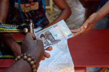 African hands exchanging cash, money or the Nigerian currency know as Naira in a tailoring shop for business purpose and with a sewing machine in the background
