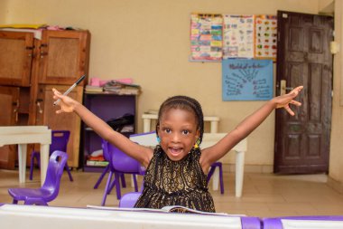 A cute african girl child studying alone in a classroom with her books on a colorful desk as she prepares for excellence in her schooling, education and career