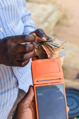 Picture of african hands counting cash, money, or Nigerian currency while another hand is holding a digital point of sales machine which is known as POS device
