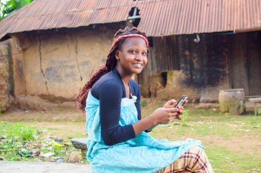 Köyün çamurlu evinin önünde oturan mutlu bir kadın ya da kadın akıllı bir telefon kullanıyor.