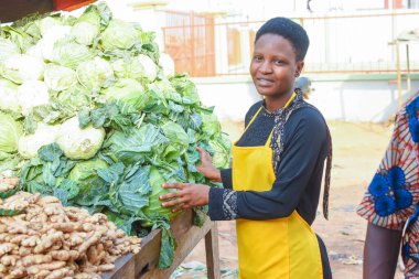 Happy African business woman or female trader wearing a yellow apron and standing at her stall in a market