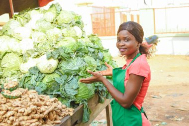 Happy African business woman or female trader wearing a green apron and standing at her stall in a market