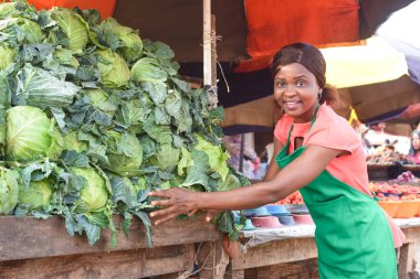 Happy African business woman or female trader wearing a green apron and tending to her goods of vegetables in a market place