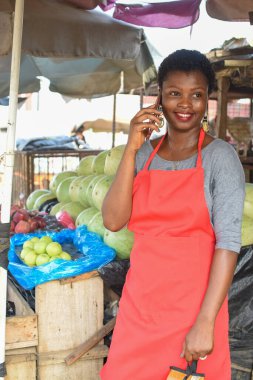 Afrikalı kadın ya da kadın tüccar, marketteki tezgahında dururken akıllı bir telefonla arıyor.