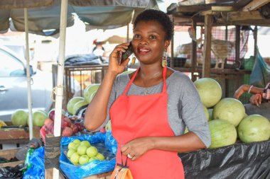 Afrikalı kadın ya da kadın tüccar, marketteki tezgahında dururken akıllı bir telefonla arıyor.