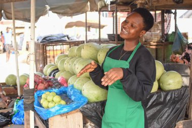 African woman or female trader with a green apron, dancing at her stall in a local market