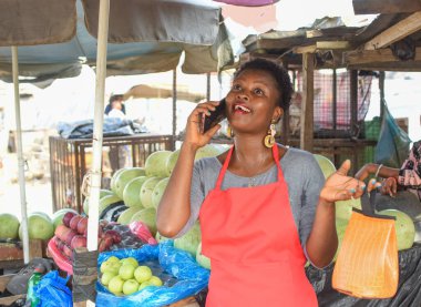 Afrikalı kadın ya da kadın tüccar, marketteki tezgahında dururken akıllı bir telefonla arıyor.