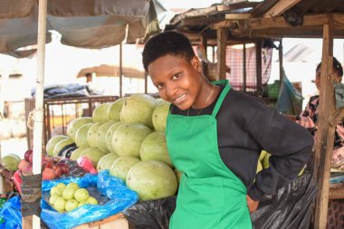 Yeşil önlüklü Afrikalı kadın ya da kadın tüccar, yerel bir markette tezgahında duruyor ve alıcılara satmaya hazırlanıyor.