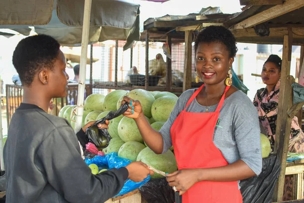 African woman or female trader in red apron selling her goods to a customer in a local market