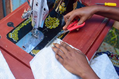 African hands of a female tailor or fashion designer making a dress with a sewing machine in a tailoring shop while working with a scissors