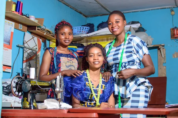 Üç Afrikalı Nijeryalı kadın terzi, moda tasarımcıları, iş kadınları ya da girişimciler bir terzide kameraya mutlu bir şekilde bakıyorlar.