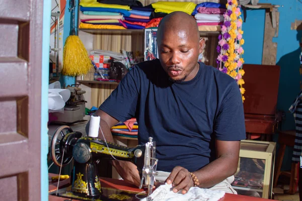 African Nigerian male tailor, fashion designer or business man working with a sewing machine in a tailoring shop