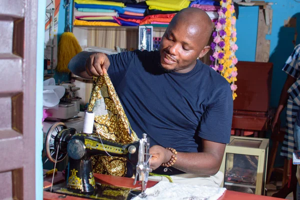 A happy African Nigerian male tailor, fashion designer or business man working with a sewing machine in a tailoring shop