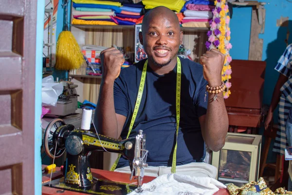 A happy African Nigerian male tailor, fashion designer or business man working with a sewing machine in a tailoring shop