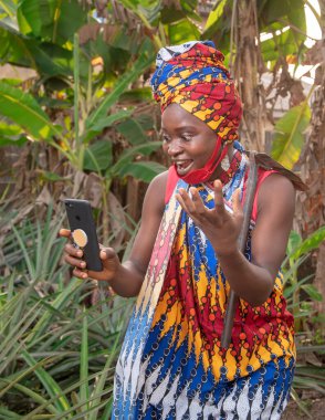  Güzel, mutlu bir Afrikalı kadın çiftçi. Burun maskeli. Ananas ve muz çiftliğinde omzundan sarkan çapayla akıllı bir telefon tutuyor. 