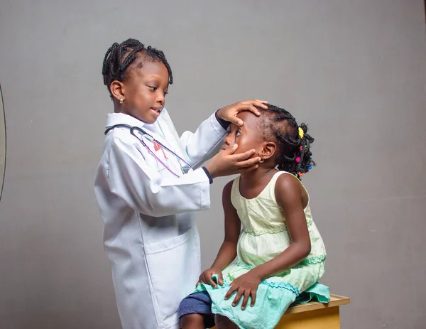 African Nigerian girl child with stethoscope, playing medical expert like doctor and nurse with kid patient sitting in front of her