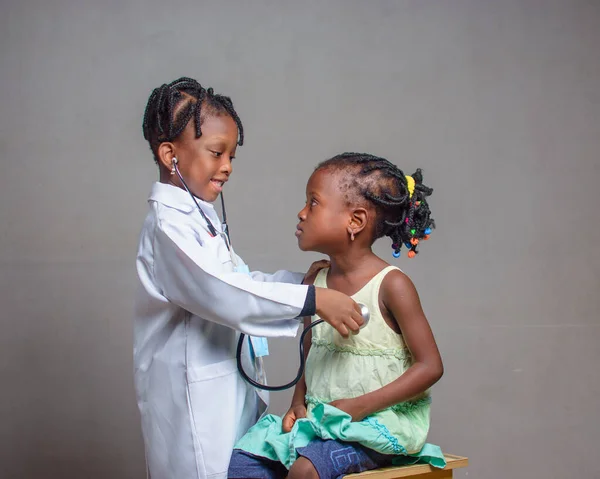 African Nigerian girl child with stethoscope, playing medical expert like doctor and nurse with kid patient sitting in front of her