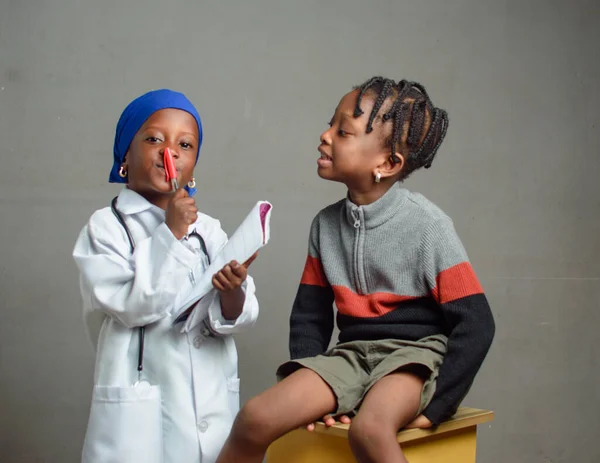 African Nigerian girl child with stethoscope, playing medical expert like doctor and nurse with kid patient sitting in front of her