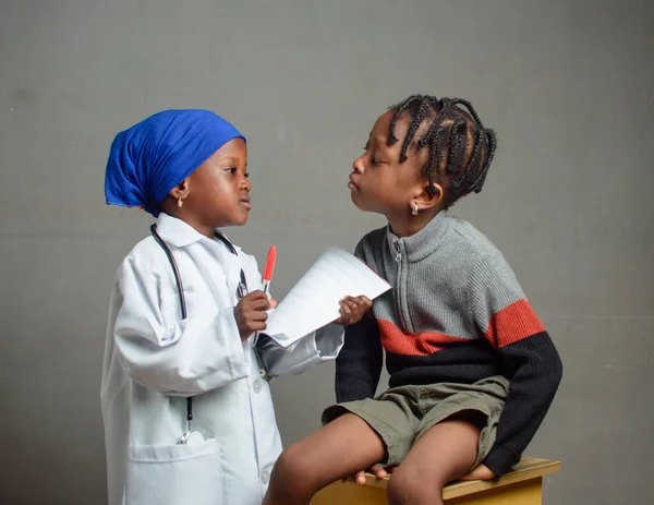 African Nigerian girl with stethoscope, playing medical expert like doctor and nurse with kid patient sitting in front of her