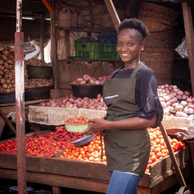 A beautiful and happy African Nigerian female trader, seller, business woman or shop owner preparing to sell goods to her customers in a market