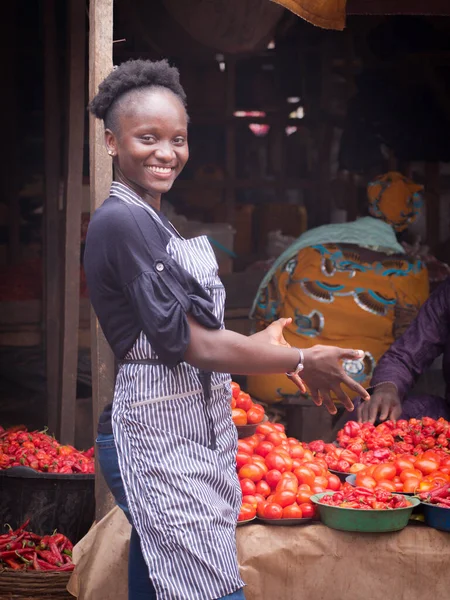 An African Nigerian female trader, seller, business woman or entrepreneur with an apron, happily showing her displayed goods to attract potential customers in a market