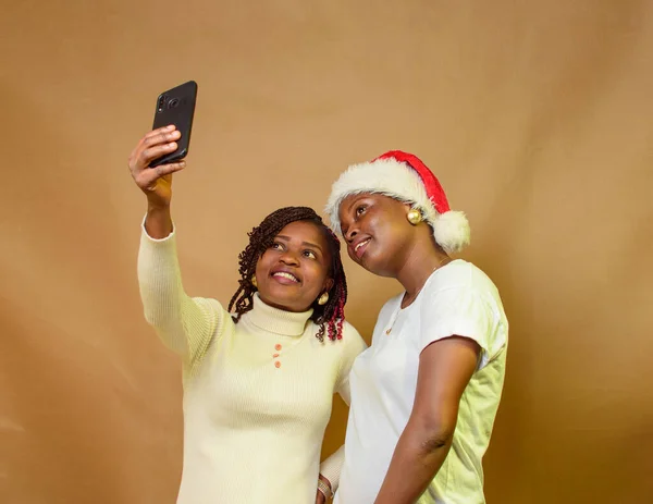 Two African ladies, sisters or friends taking photographs with a smart phone while one of them have a Christmas cap on her head