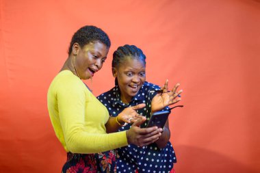 Two joyful African Nigerian women, ladies, sisters or friends happily looking into a smart phone