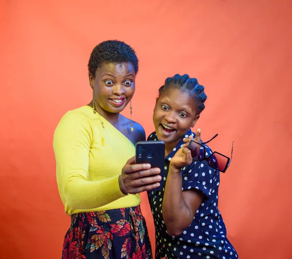 Two joyful African Nigerian women, ladies, sisters or friends happily looking into a smart phone