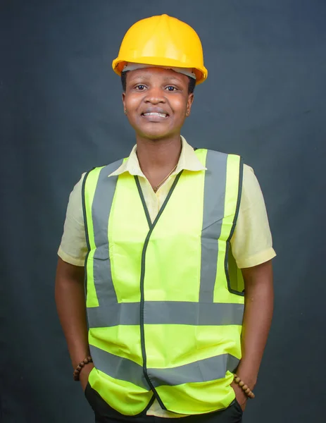 African Nigerian female construction or civil engineer, architect or builder with yellow safety helmet and green reflective jacket