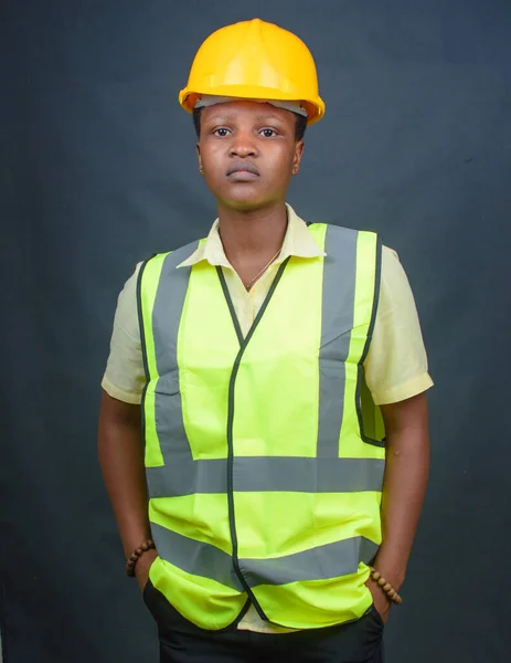African Nigerian female construction or civil engineer, architect or builder with yellow safety helmet and green reflective jacket