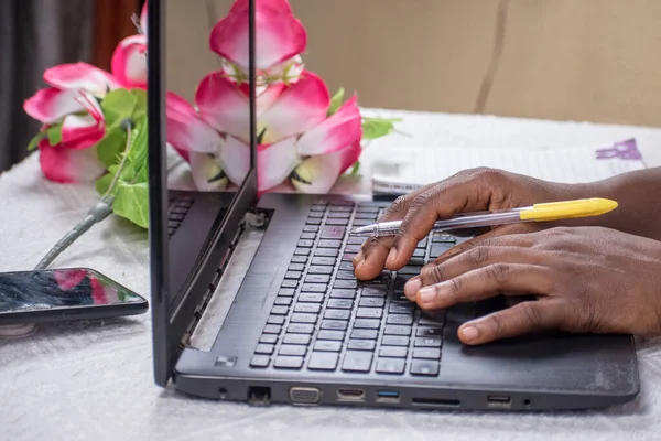 African hands holding a pen and typing on a black laptop\'s keyboard