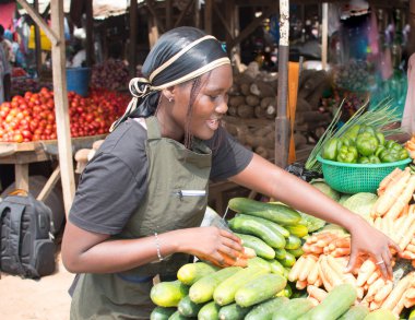 stock photo of female African grocery seller or business woman with apron, standing at her stall in a market, ready to sell to customers