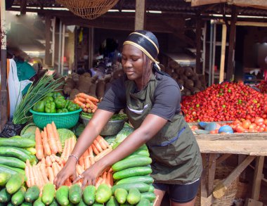 stock photo of female African grocery seller or business woman with apron, standing at her stall in a market, ready to sell to customers