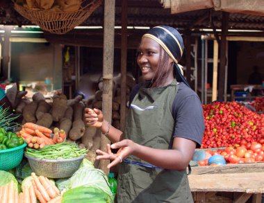 stock photo of female African grocery seller or business woman with apron, standing at her stall in a market, ready to sell to customers