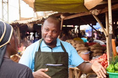 stock photo of male African grocery seller or business man with apron, standing at his stall in a market, ready to sell to customers