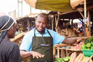 stock photo of male African grocery seller or business man with apron, standing at his stall in a market, ready to sell to customers