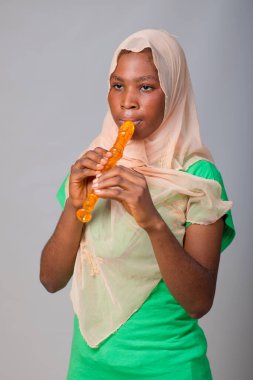 African Nigerian Muslim lady, girl or music student wearing an hijab head scarf and blowing musical instrument called flute