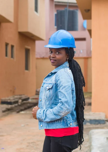 Outdoor portrait of a cute African lady or woman from Nigeria with blue safety helmet representing industrial professionals like construction specialist, builders, architect and engineer