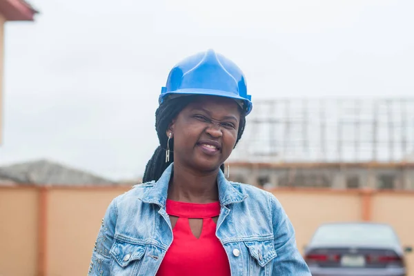 Outdoor portrait of a cute African lady or woman from Nigeria with blue safety helmet representing industrial professionals like construction specialist, builders, architect and engineer