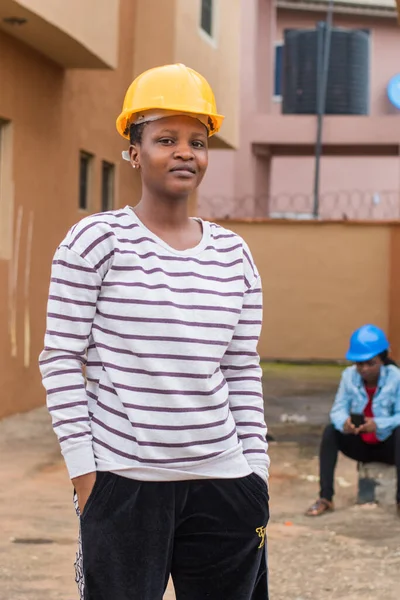 Outdoor portrait of a cute African lady or woman from Nigeria with yellow safety helmet representing industrial professionals like construction specialist, builders, architect and engineer