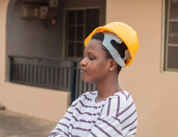 A cute African lady or woman from Nigeria with yellow safety helmet wrongly placed on her head as she represent industrial professionals like construction specialist, builders, architect and engineer